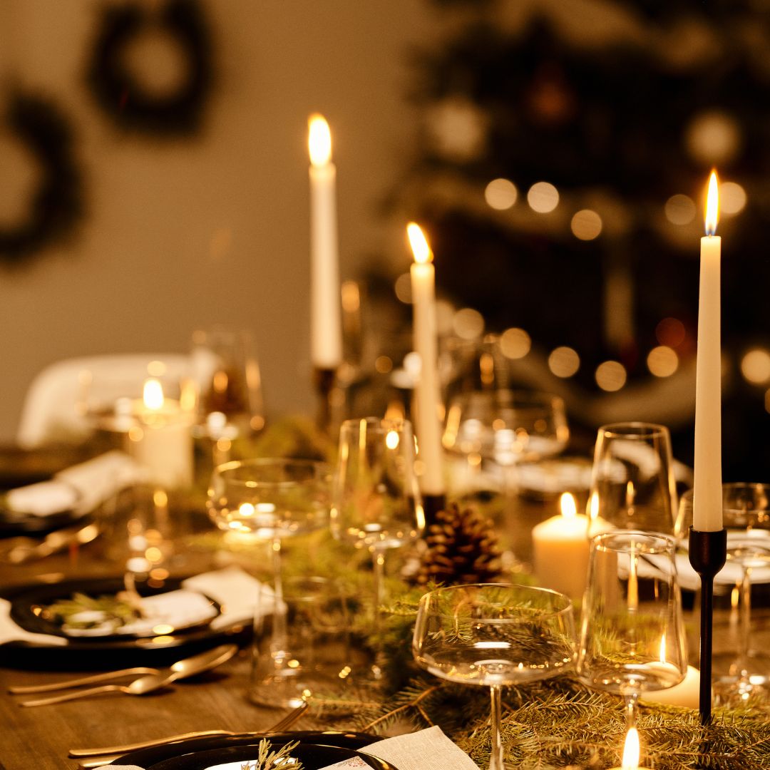 A festive table with a colourful bowl of roasted vegetables, a jug of sparkling water with orange slices and two glasses, one of red wine and one alcohol-free.