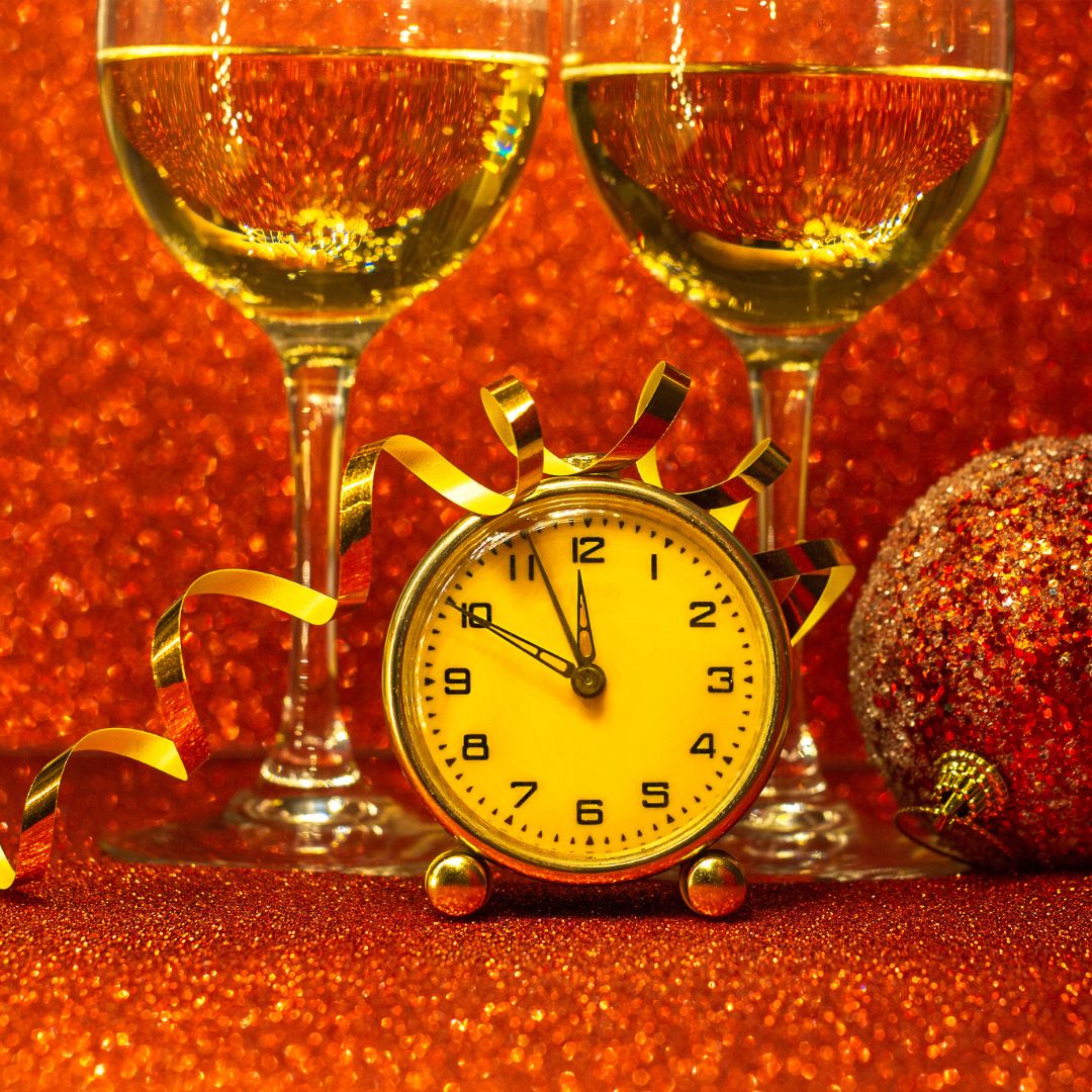 A glass of red wine on a bedside table beside a softly lit lamp and an alarm clock showing 3am.