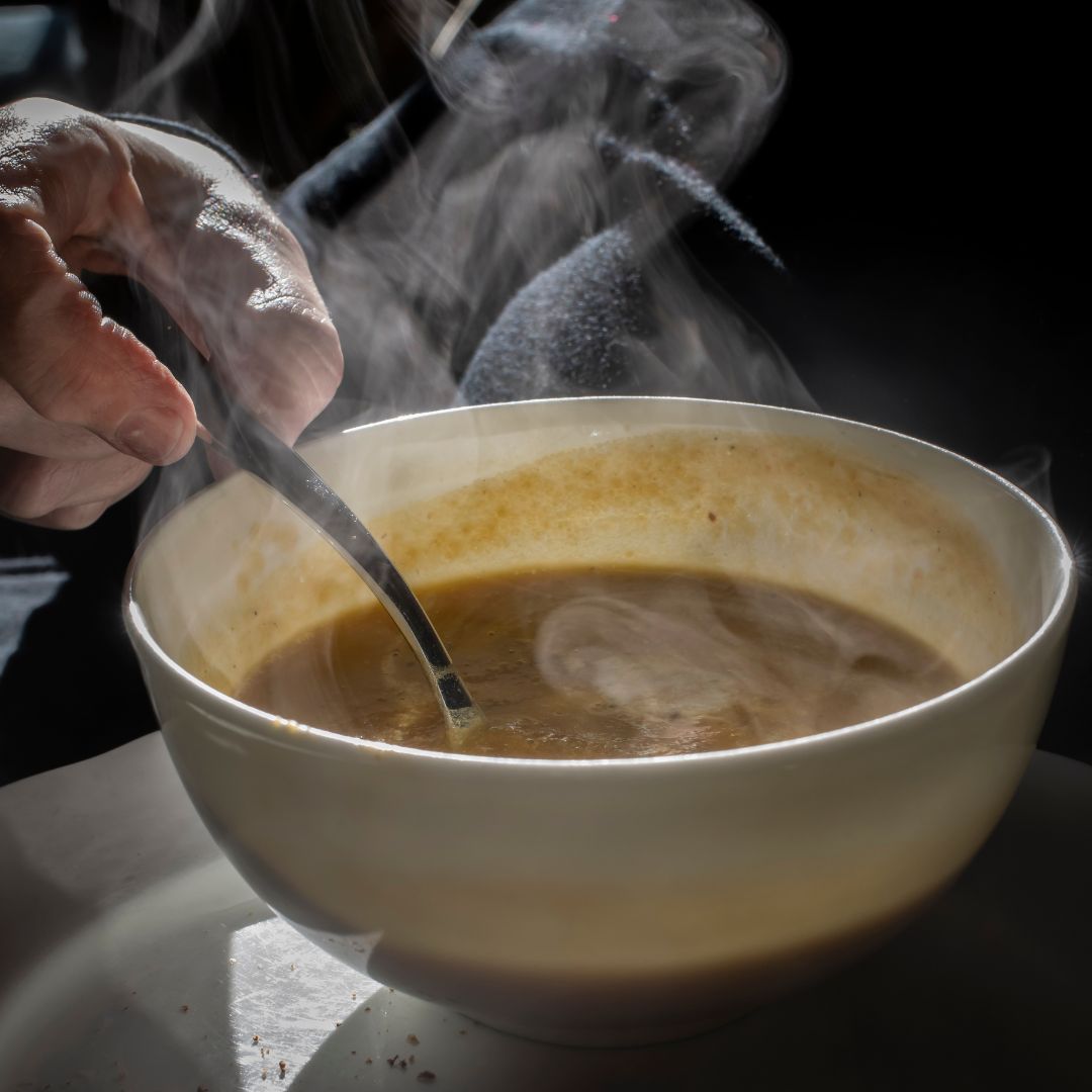 Steaming bowl of garlic and ginger broth with herbs, served in winter setting.