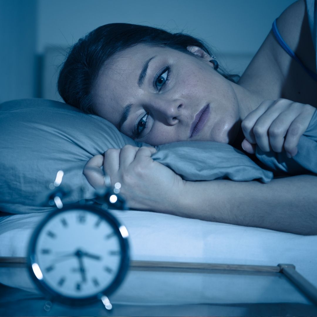 Woman awake in bed at night after feeling tired during the day, illustrating disrupted sleep and circadian rhythm.